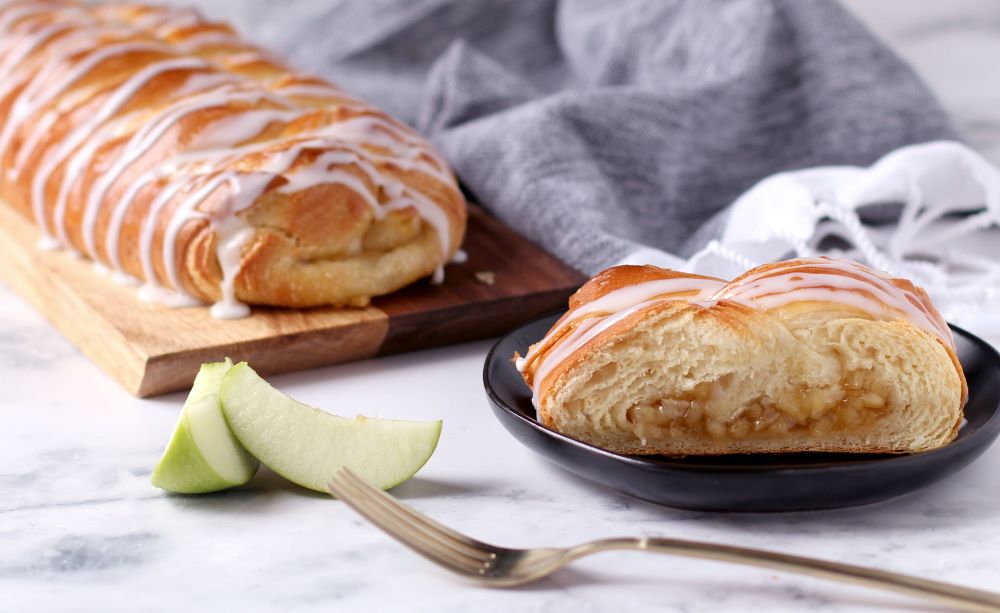 Butter Braid Apple Pastry slice on a plate with a full pastry in the background.