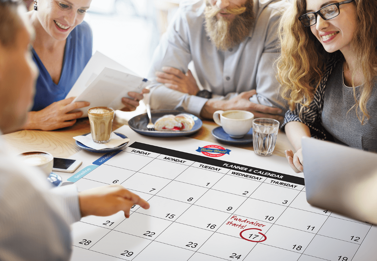 Group of people around a calendar with coffee and pastries talking about Butter Braid® Fundraising programs.