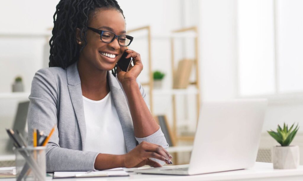 Woman talking on her cell phone while working on a laptop in an office.
